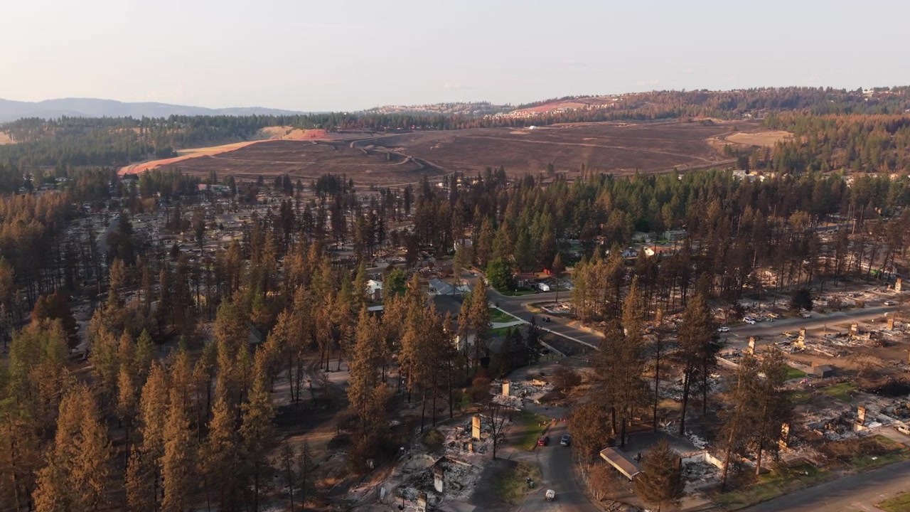 Danni dell'incendio Spokane Old Trails mostrati in un ampio sorvolo aereo su case bruciate, lotti carbonizzati, alberi anneriti e diffusa distruzione residenziale dopo l'incendio boschivo del 2026.