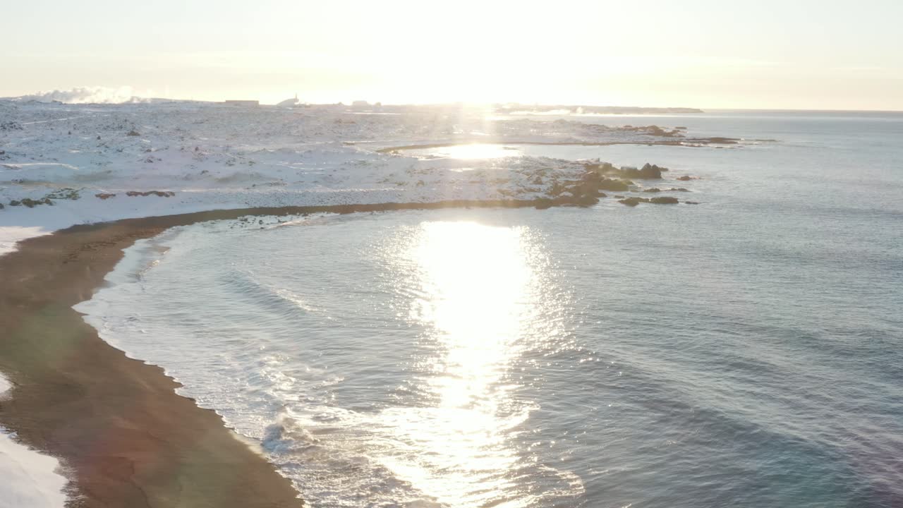 sandvik에서 눈으로 덮인 아이슬란드 해안 위로 밝은 한낮의 태양이 빛난다