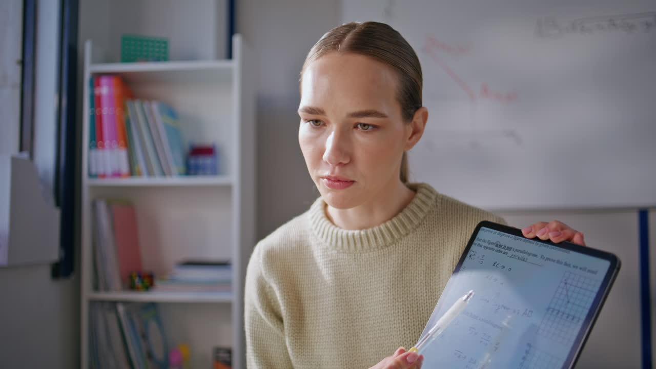 Young teacher explaining online lesson pointing tablet at class room closeup