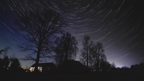 kilka gwiazd okrąża czyste niebo za wysokimi drzewami, gdy na litewskiej wsi zapada noc