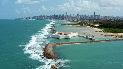 tilting up aerial drone shot of the historic star shaped reis magos fort built on a reef with the coastal capital city of natal in rio grande do norte, brazil in the background on a warm summer day