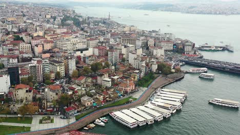 Amplia-Vista-Aérea-De-Taksim-Y-Karakoy-En-Estambul,-Turquía,-Con-Transbordadores-Atracados-En-La-Costa-Del-Río-Bósforo-En-Una-Mañana-Nublada-Rodeada-De-Viejos-Edificios-Europeos