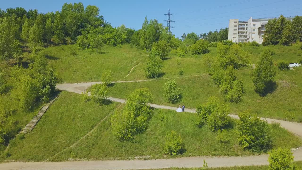 lejana pareja recién casada en la colina curva de la carretera vista de pájaro