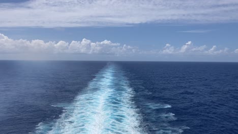 wake behind large ship on the ocean with sunny blue sky and clouds on horizon