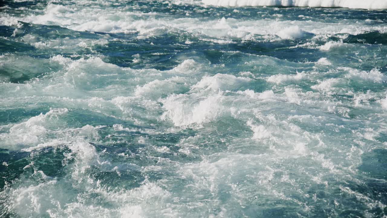 Le onde si infrangono energicamente contro una costa frastagliata, sollevando spruzzi d'acqua in aria. Le vivaci acque blu creano uno sfondo mozzafiato sotto un cielo terso.