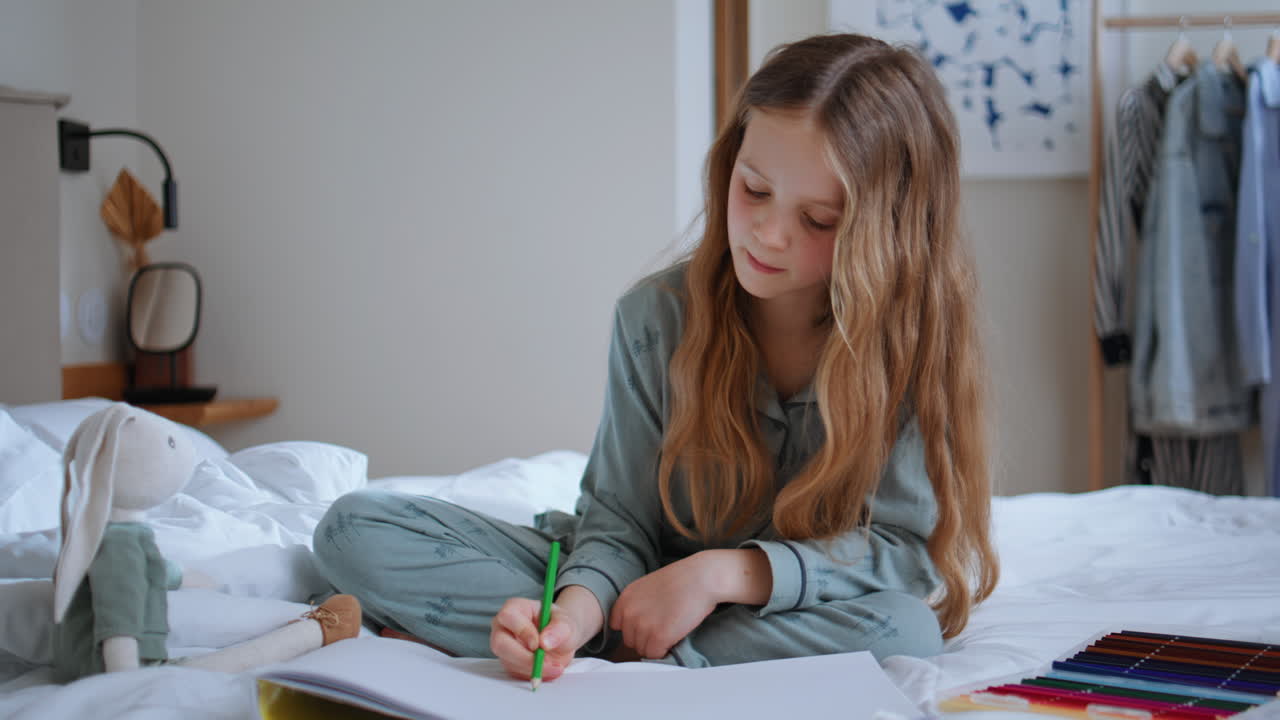 Child girl drawing picture sitting bed at home. Little toddler painting pencil