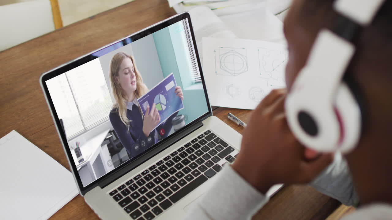 hombre de negocios afroamericano sentado en un escritorio usando una computadora portátil haciendo una videollamada con una colega
