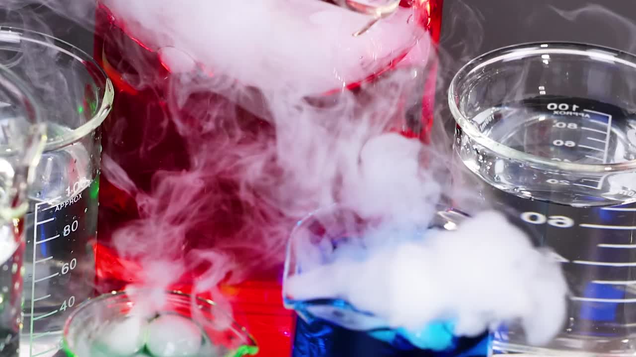 Close-up of colorful liquids reacting with smoke and bubbles in laboratory glassware.