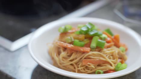 Fideos-De-Espagueti-Con-Pimientos-Cocidos-En-Rodajas-De-Colores,-Zanahorias-Y-Puerro-Fresco-Con-Salsa-De-Maní-En-Un-Plato-Humeante-De-Pentecostés