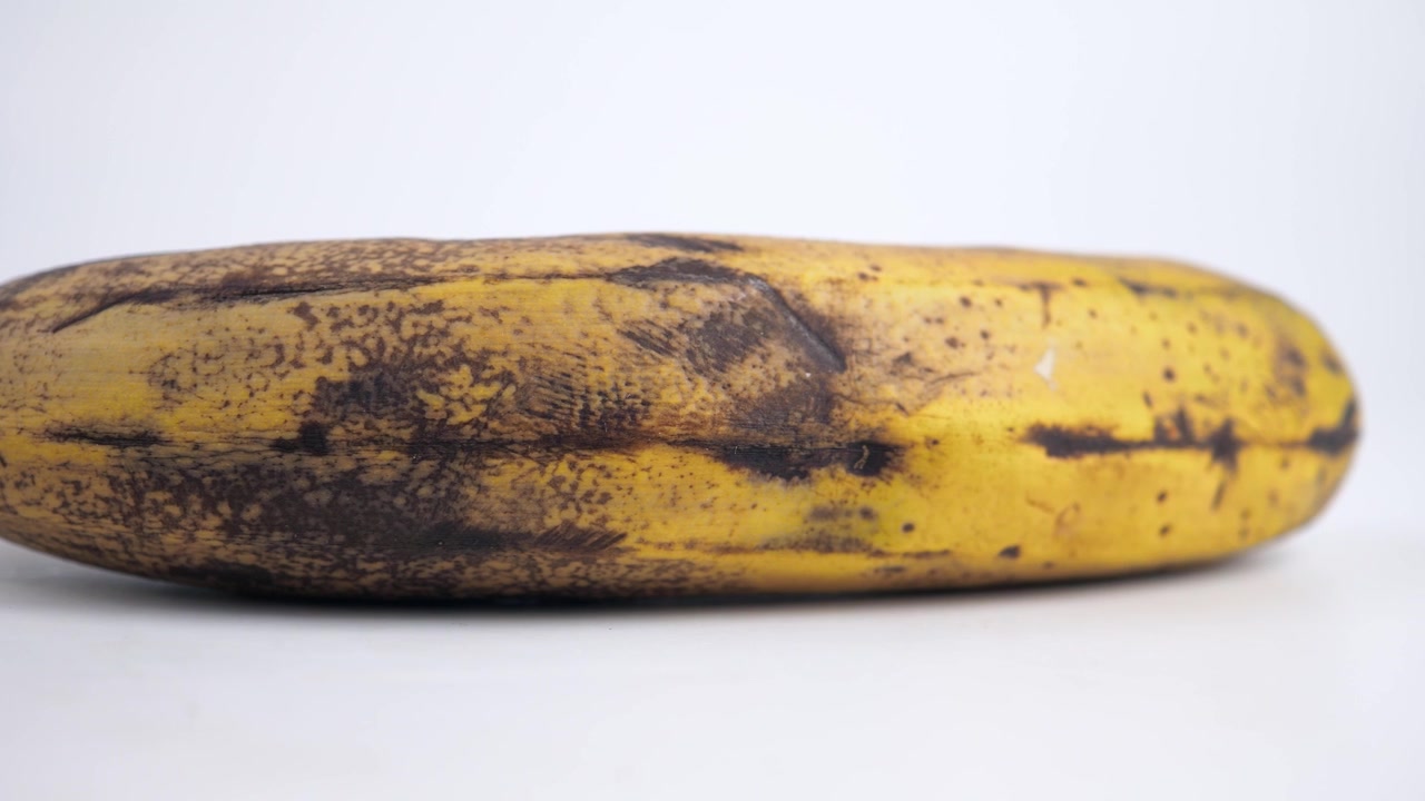 Banana troppo matura con macchie marroni su sfondo bianco