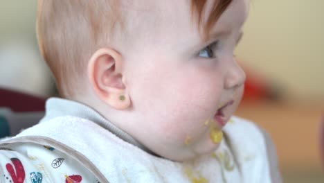 slow motion baby with dirty face of baby food looking out of plane turns his head