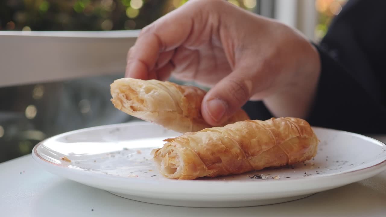 Hand Picking Up Golden Brown Pastry Roll from White Plate