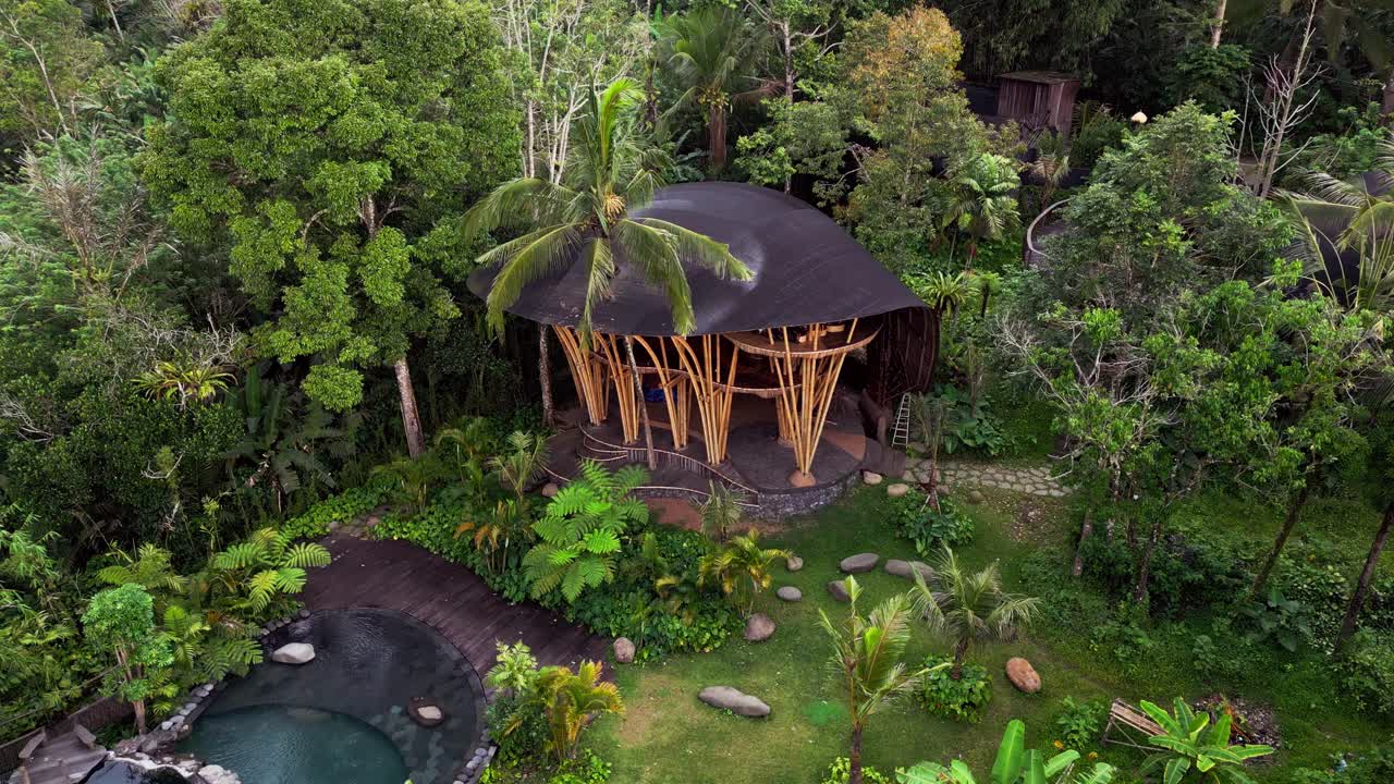 Aerial view of eco bamboo villas being built in a lush forest setting with tropical trees and a pool. The footage captures Bali’s unique harmony between design and the natural landscape