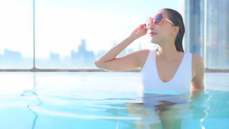 woman in a rooftop swimming pool, resting leaning on elbows and looks out over modern city skyline, title space