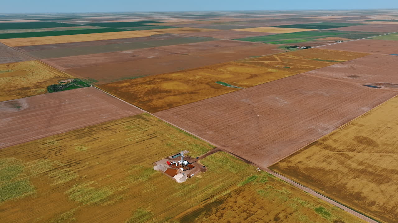 Vast rectangular fields of different colors. Approaching one of the areas with oil production site.
