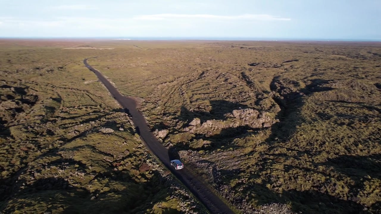 Vista aerea con drone di un campo lavico coperto di muschio lungo la Strada 864 vicino a Hljodaklettar in Islanda, con terreno vulcanico, strada tortuosa e un veicolo che attraversa il paesaggio.