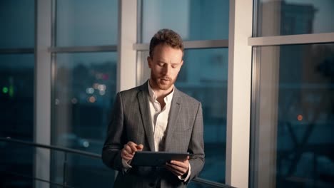 stylish young man with a tablet on a background of panoramic windows with a night city