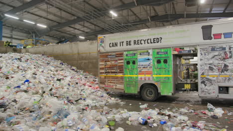 recycling truck reversing toward a pile of plastic bottles in a recycling plant