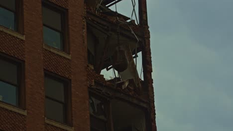 close-up shot of a wrecking ball smashing through the upper floors of a partially demolished brick high-rise during a downtown demolition project.