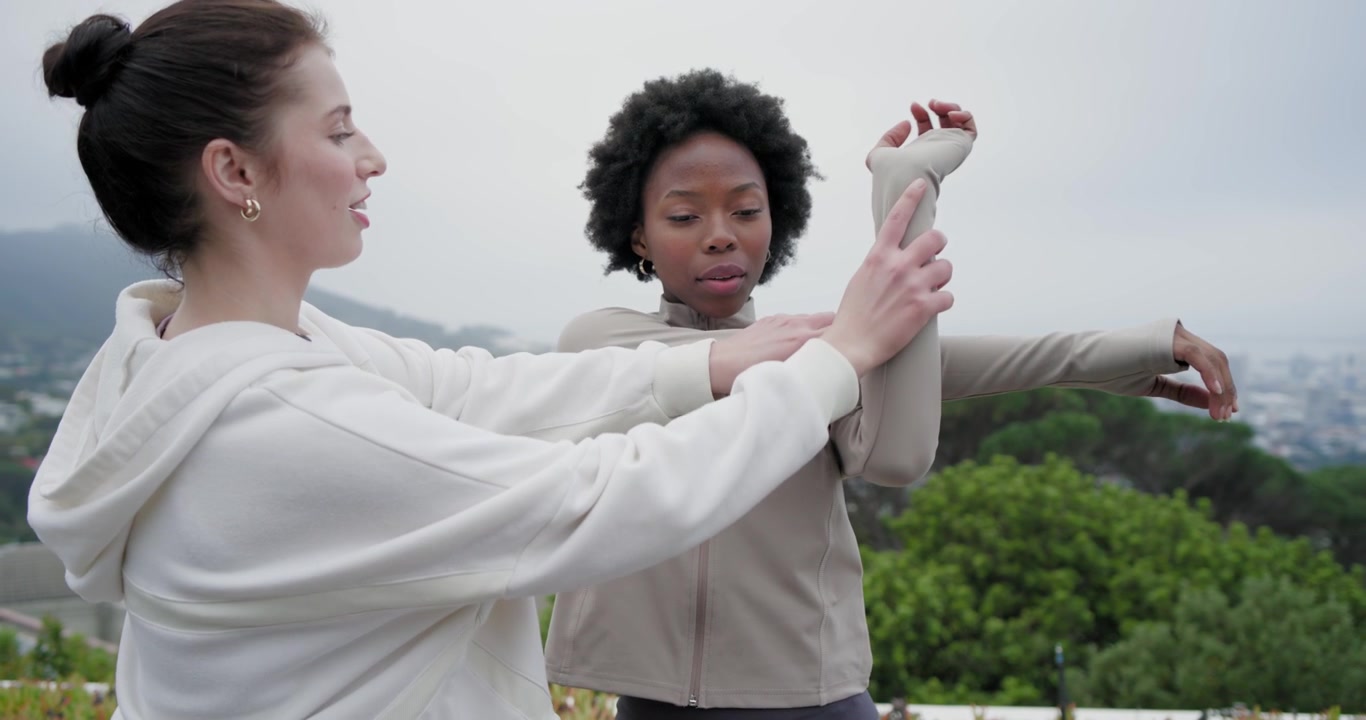 Diverse women walking rooftop deck, one raising arm, hoodie helper guiding and deepening stretch