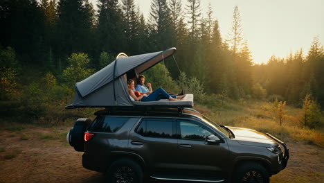 couple relaxing on a rooftop tent in a forest at sunset