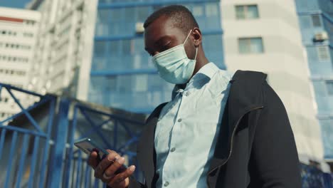 man using smartphone while wearing a mask in city