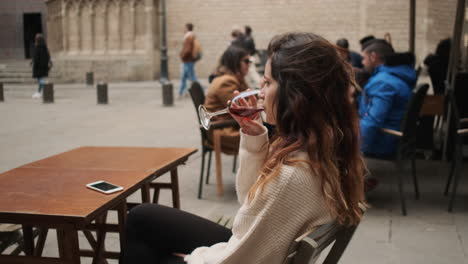 Una-Joven-Sentada-En-Un-Café-Bebiendo-Una-Copa-De-Vino-Tinto.