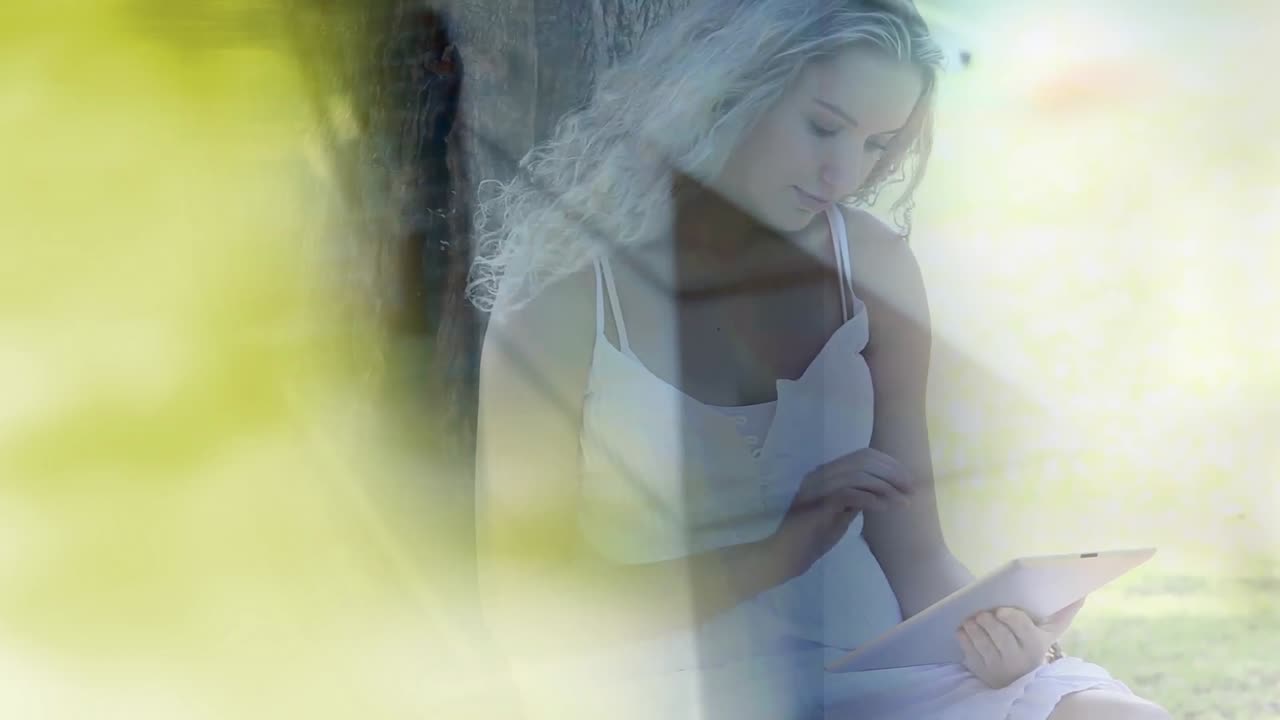 composición digital de rastros de luz amarilla contra mujer caucásica usando tableta digital en el parque