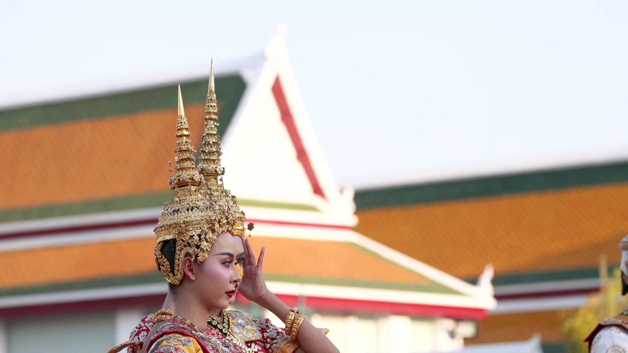 Mezza figura di un artista Khon in costume dorato che gesticola davanti a un tempio buddista