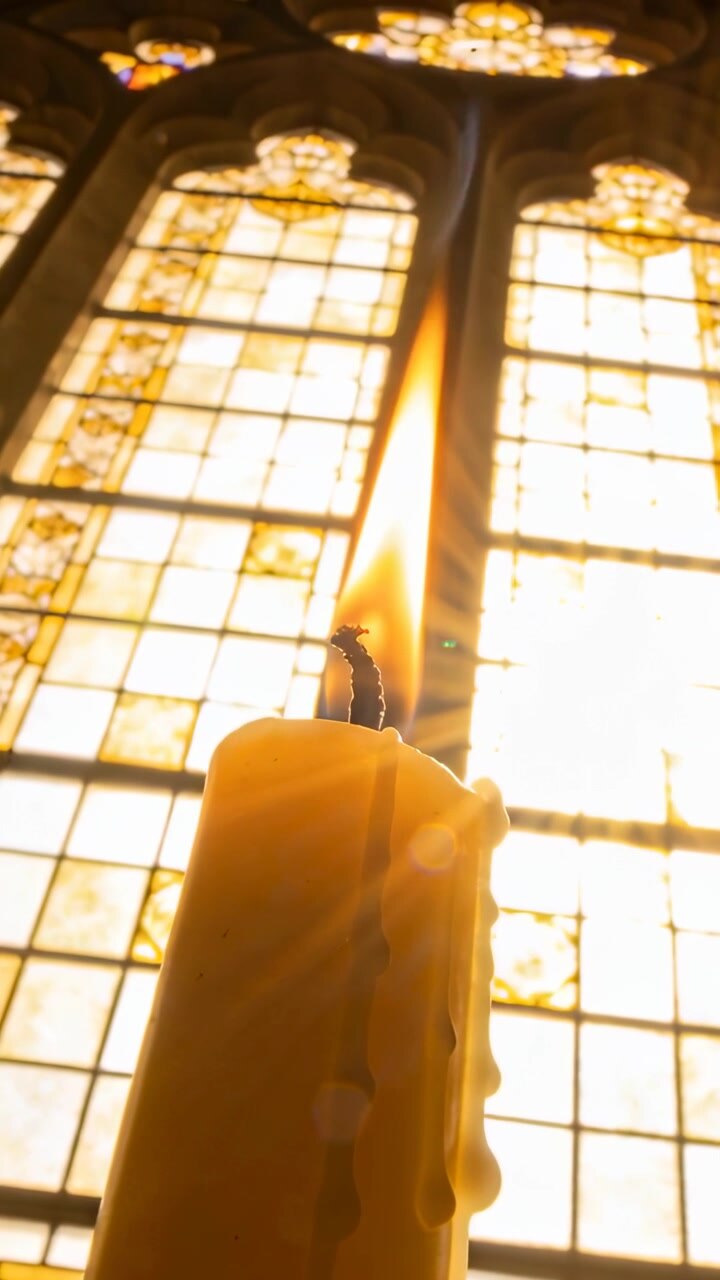 Vertical video: Melting yellow candle making drips at window with sunlight pouring, wick flickering