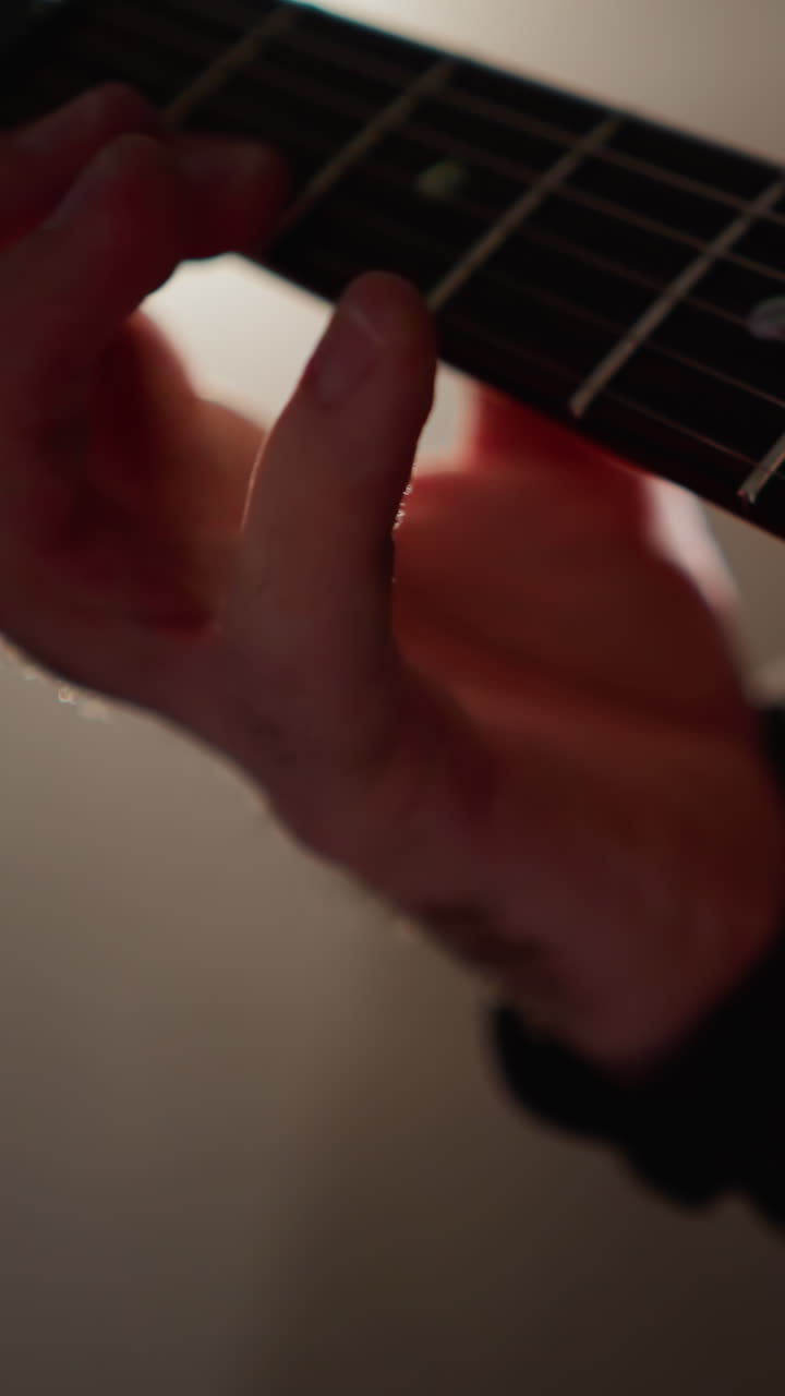 primer plano de la mano de un guitarrista tocando las cuerdas de una guitarra, resaltado por la luz enfocada en una habitación sombreada