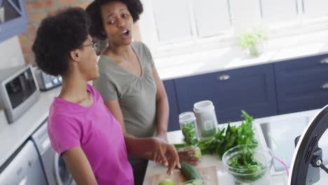 Happy-african-american-mother-and-daughter-preparing-healthy-drink,-making-video-using-smartphone