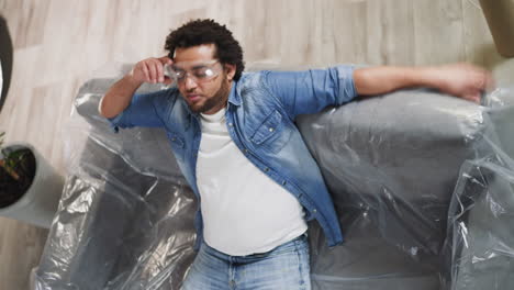 afro-american man falls down on sofa covered with plastic