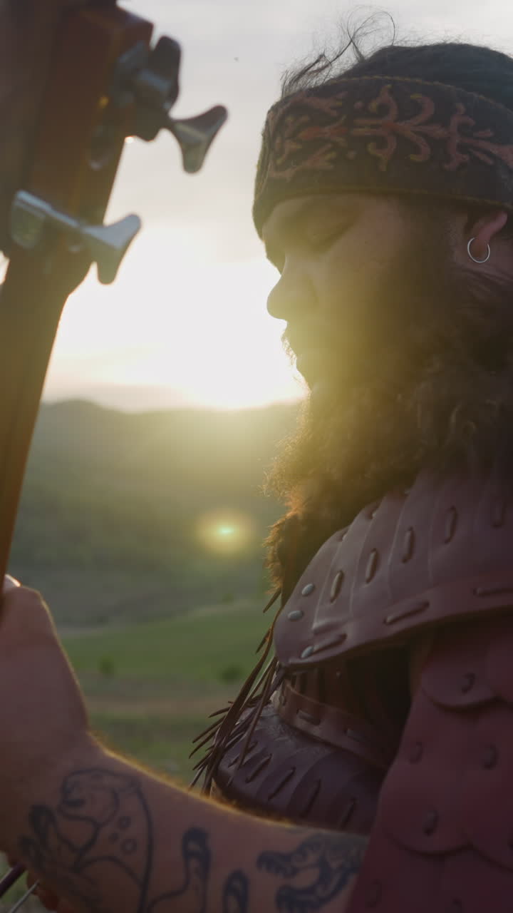 Concentrated plump musician plays igil with bow against mountain at sunrise close side view. Presenting old Altai melodies. Siberian culture festival