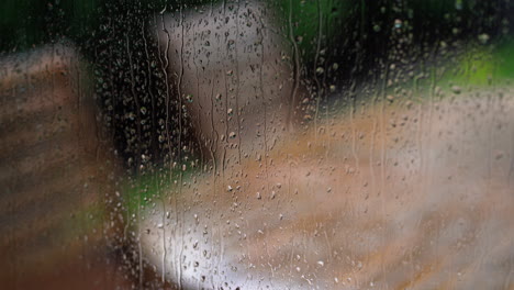 Regentropfen-Auf-Dem-Fenster-Mit-Blick-Auf-Gartentisch-Und-Stühle