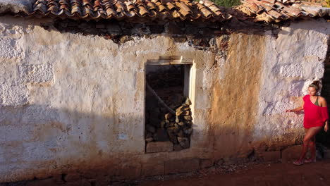 mujer con un vestido rojo mirando dentro de una casa de piedra abandonada, betancuria