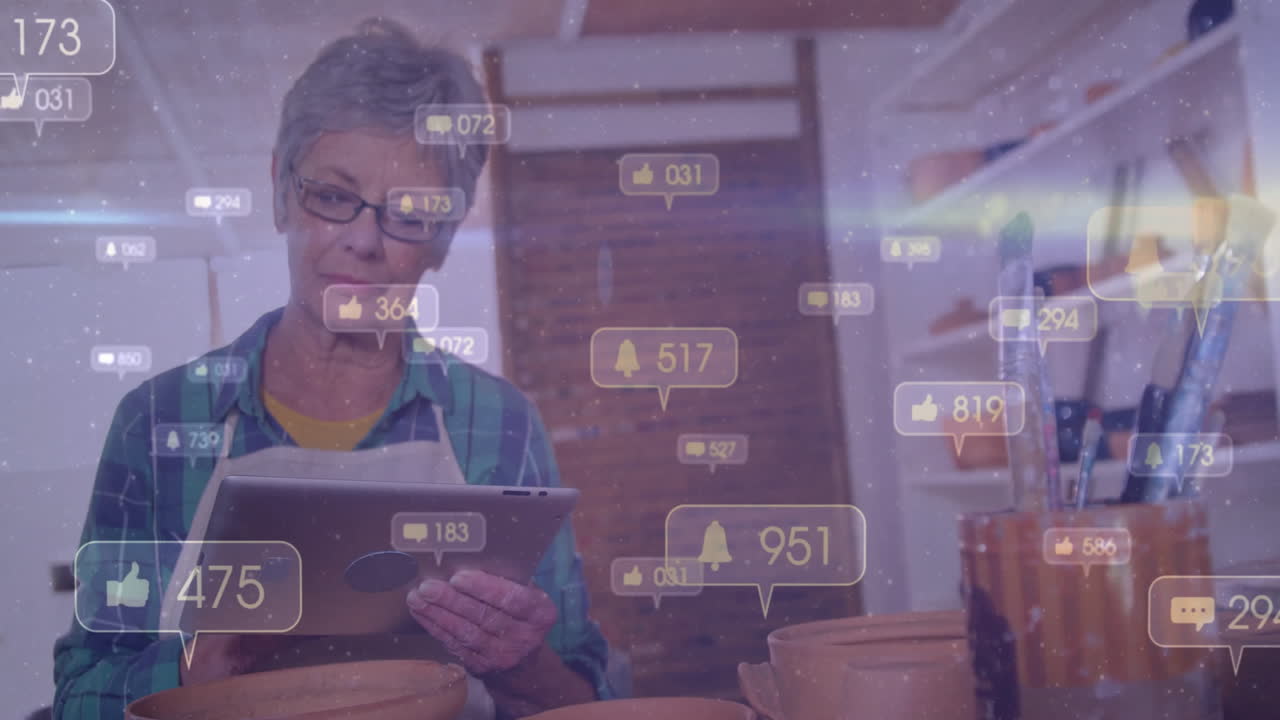 woman wearing glasses working at pottery bench using tablet, showing floating social media icons