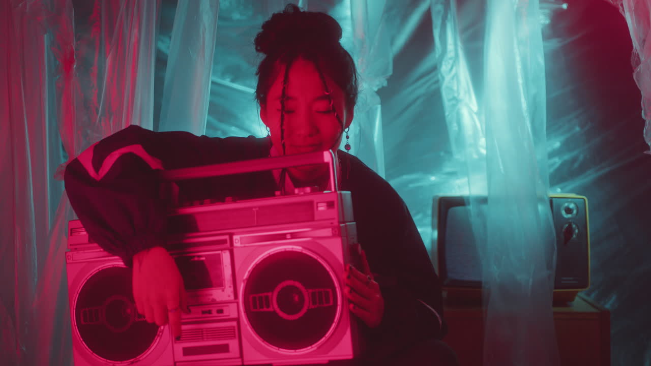 Ragazza asiatica alla moda che si gode la musica con un boombox retrò in uno studio buio con luce al neon