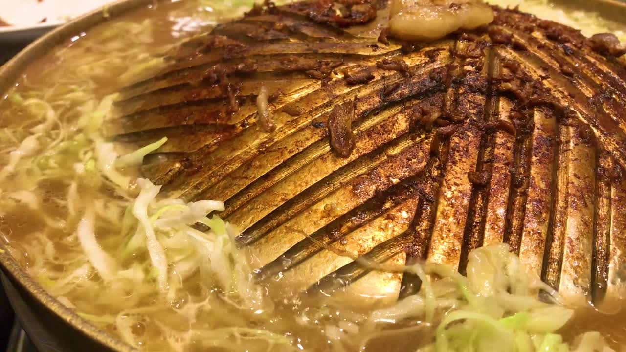 팬 주위에 수프와 야채가 끓는 황동 바비큐 팬에 있는 고기 그릴에서 탄 자국을 닫습니다.