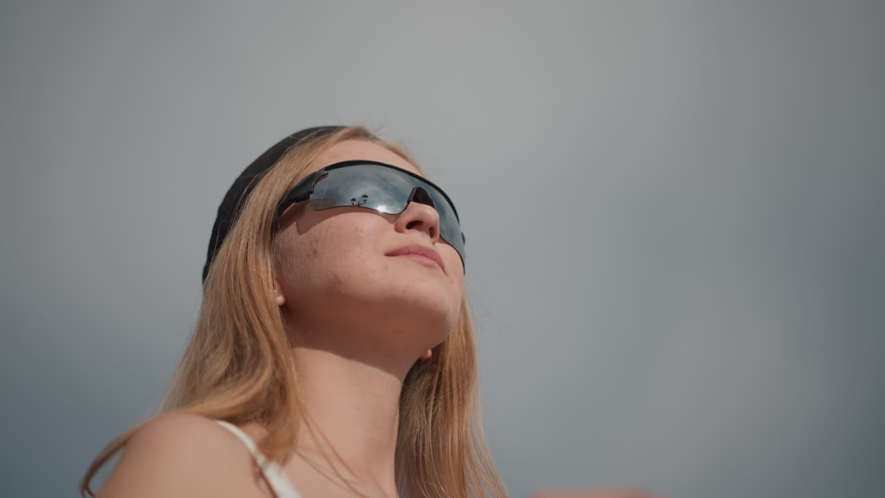 white woman adjusting sunglasses against sky, beanieclad closeups show blonde hair, freckles, upward gaze and sunlit skin confident pose with architectural backdrop, rooftop and skyline glimpses