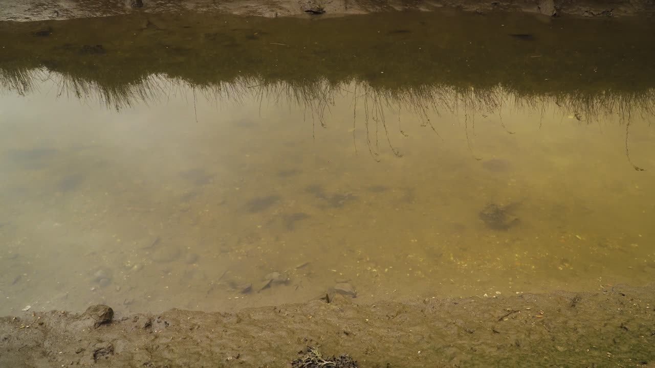 4K muddy river bed in a low tide with some water flowing down the river to the ocean