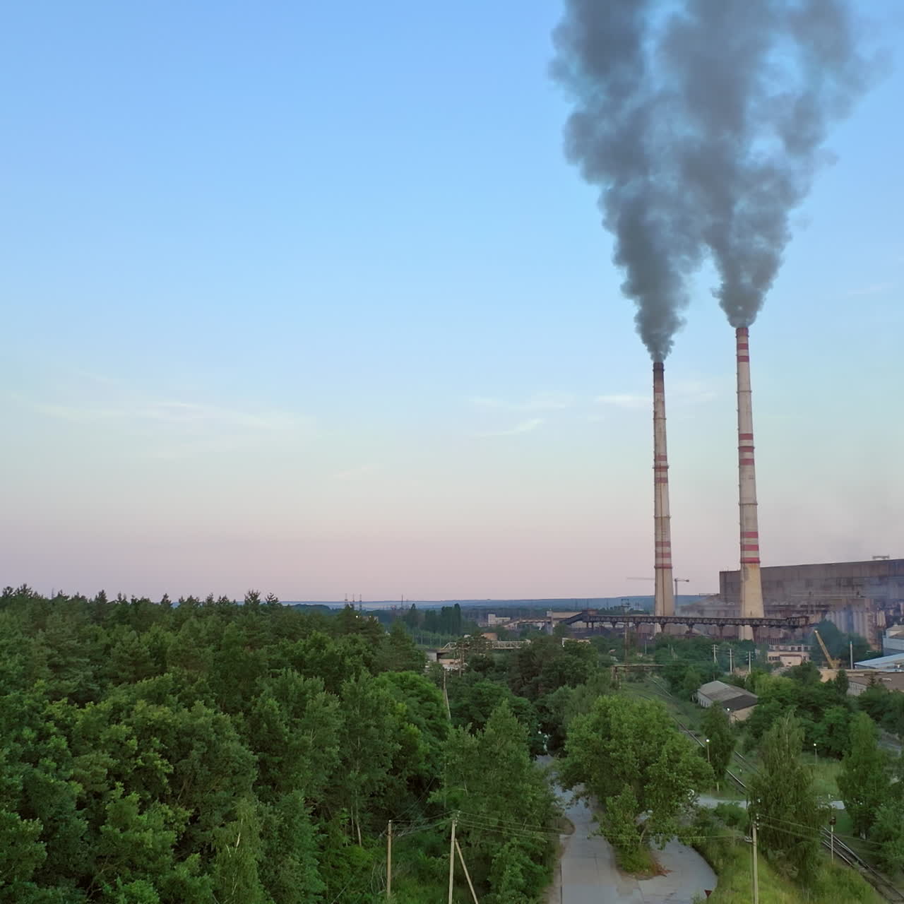 Cityscape background with two big pipes with smoke from factory. Dark smoke comes from industrial pipes near green trees. Pollution of the environment.