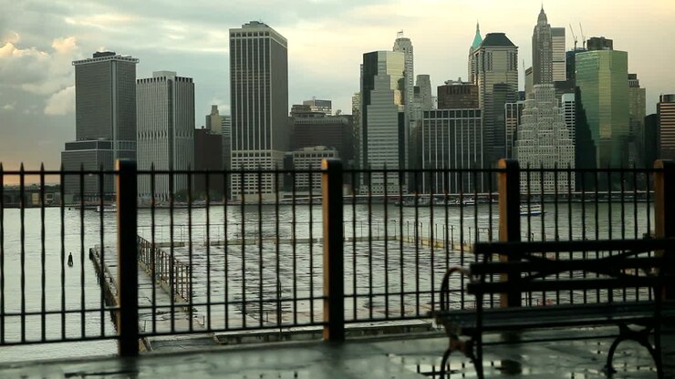 Carrellata della skyline di New York City attraverso l'East River da Brooklyn con una panchina del parco in primo piano