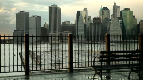 dolly shot of new york city skyline across the east river from brooklyn with a park bench in the foreground.