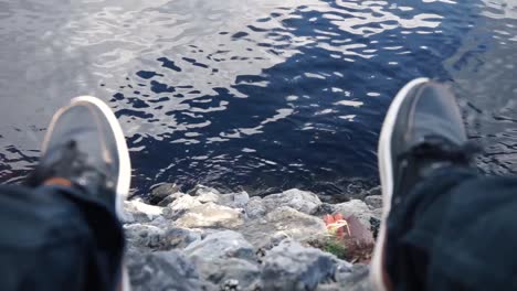 Legs-Dangling-Off-of-Face-Of-Rocks-Overlooking-Water