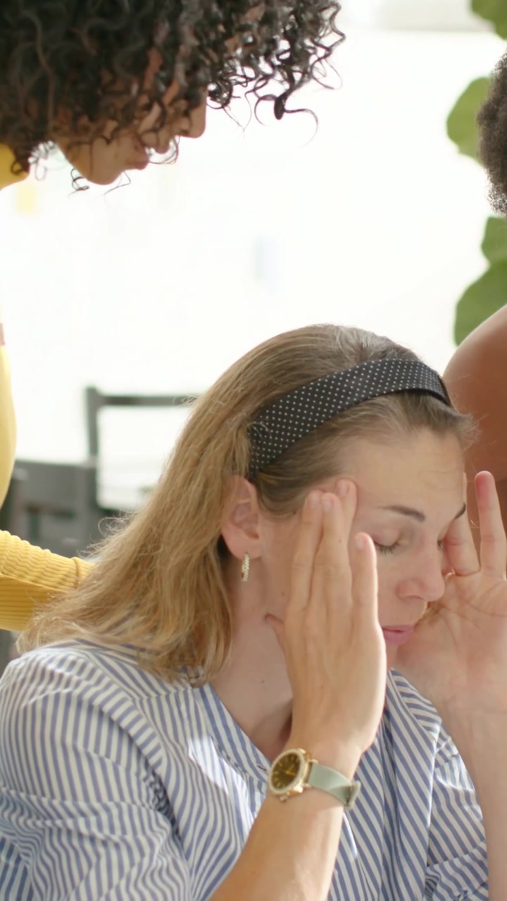 Video verticale: Donna stressata con una camicia a righe che si preme le tempie e si copre il viso alla scrivania, con una pianta.