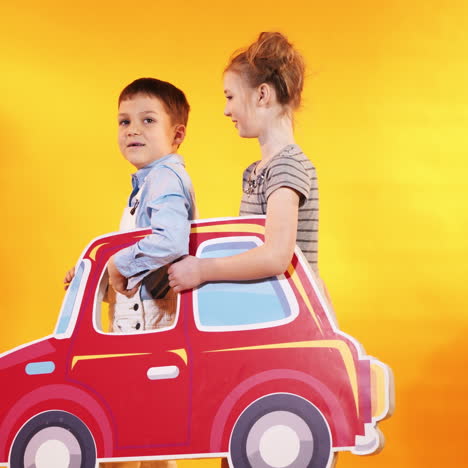 happy children with a big toy car on a bright yellow wall background. children's scenery in the studio