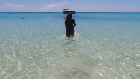 una mujer hispana de pelo largo camina lentamente hacia el claro y cálido mar del caribe.