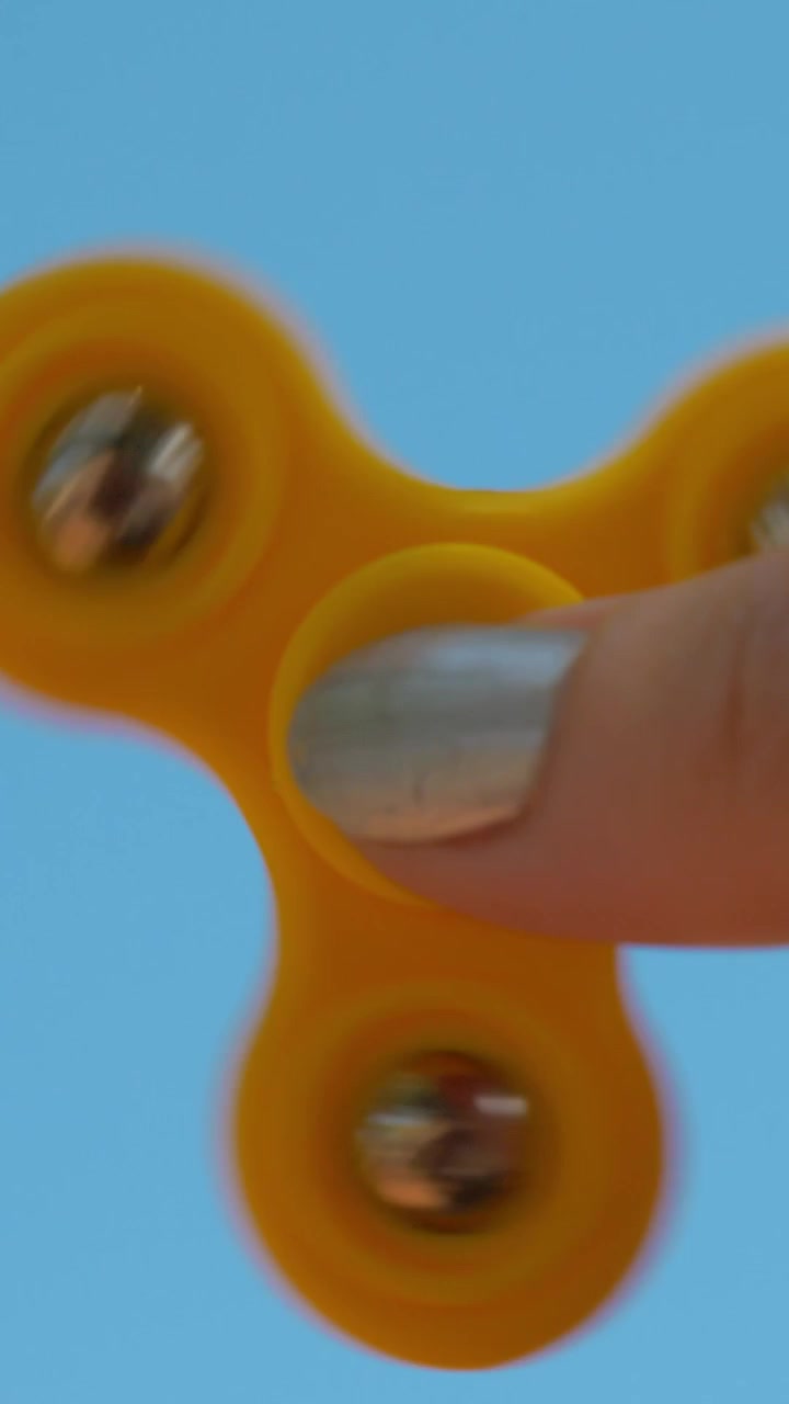 Playing with yellow fidget spinner on sky background