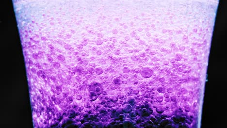 macro shot of sparkling violet bubbles floating around in a glass with bright background